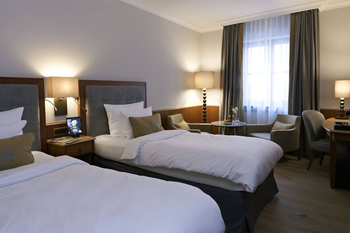 Habitación de hotel con dos camas, un escritorio, una silla, una lámpara y un televisor.