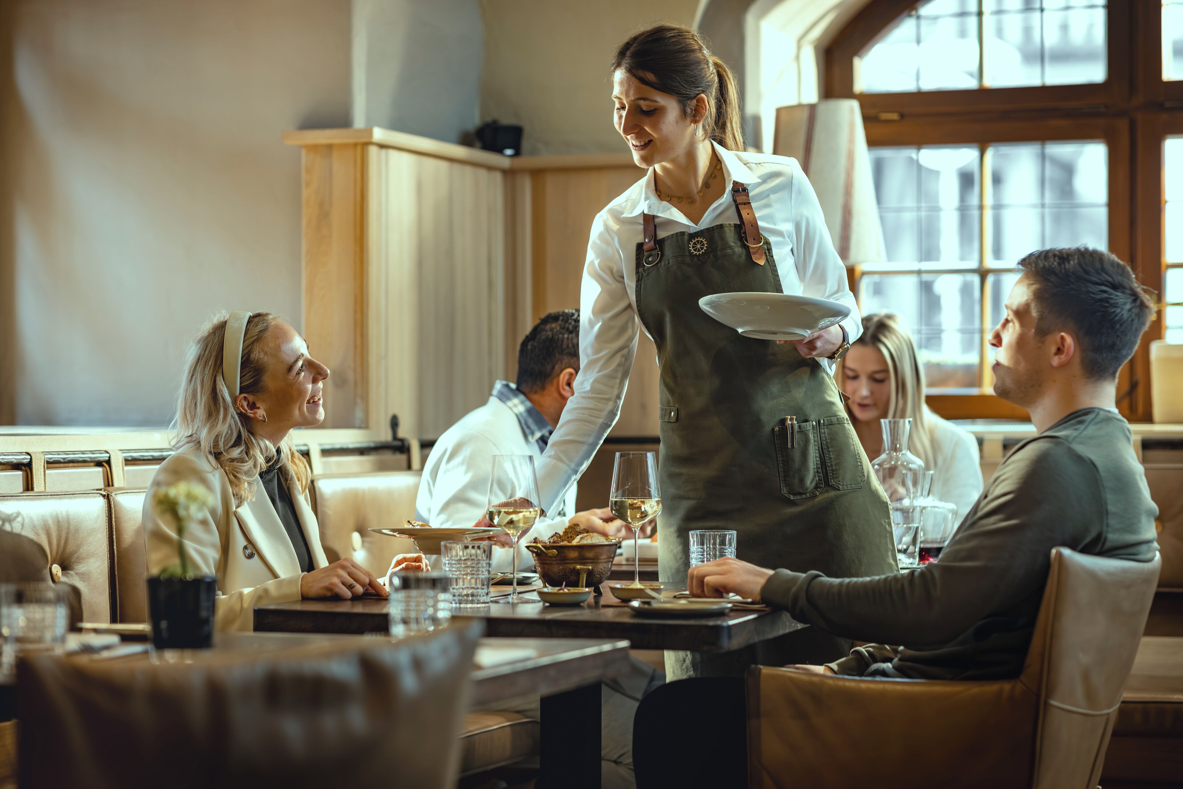 A restaurant with a waiter serving food to guests seated at tables.