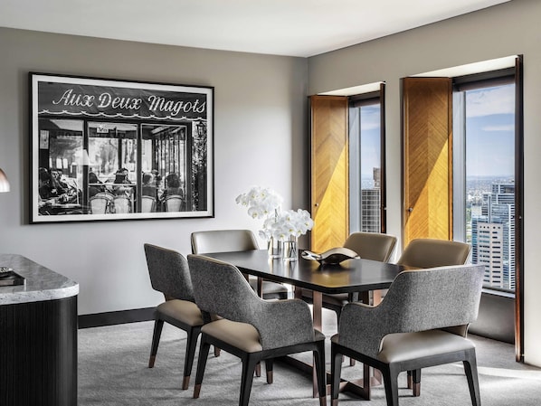 A modern hotel room with a dining area featuring a round table and four chairs, a framed black and white photo on the wall, and large windows with curtains. - Sofitel Melbourne On Collins (Melbourne)