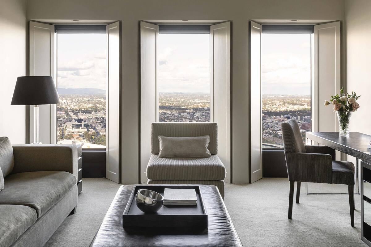 Una sala de estar moderna con un sofá, una butaca, una mesa de centro y vistas a un paisaje urbano a través de amplios ventanales.