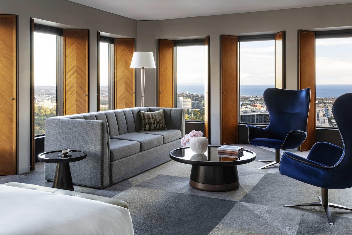 A modern hotel room with a sofa, armchair, coffee table, and a view of the city and sea.
