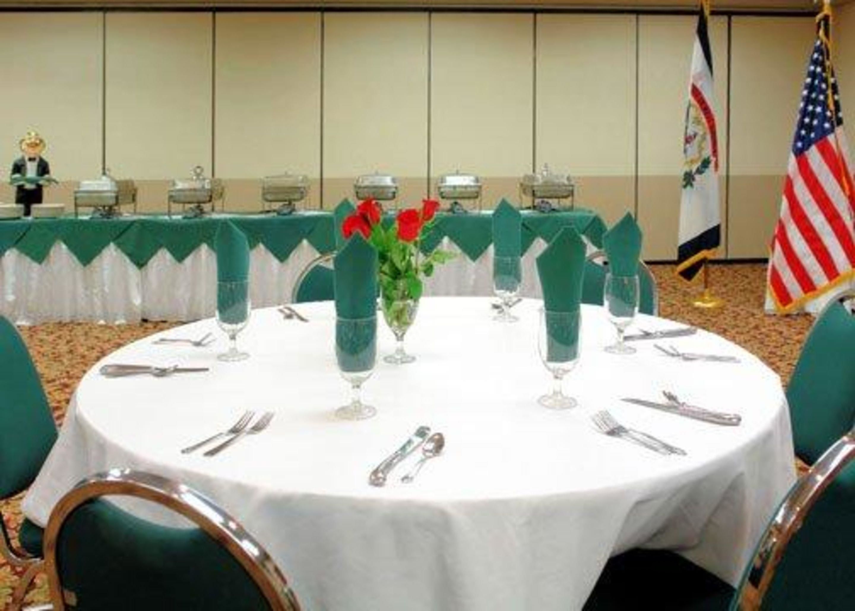 Uma sala de conferências com mesas redondas preparadas para uma reunião, cada uma com toalha branca, talheres e cadeiras verdes.