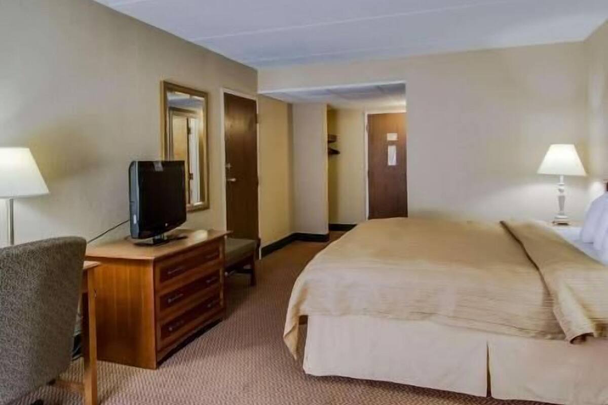 A hotel room with a bed, a television on a wooden dresser, a desk, and two lamps.
