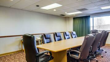 Sala de conferências com uma mesa comprida e seis cadeiras, chão coberto de carpete e uma janela com cortinas.