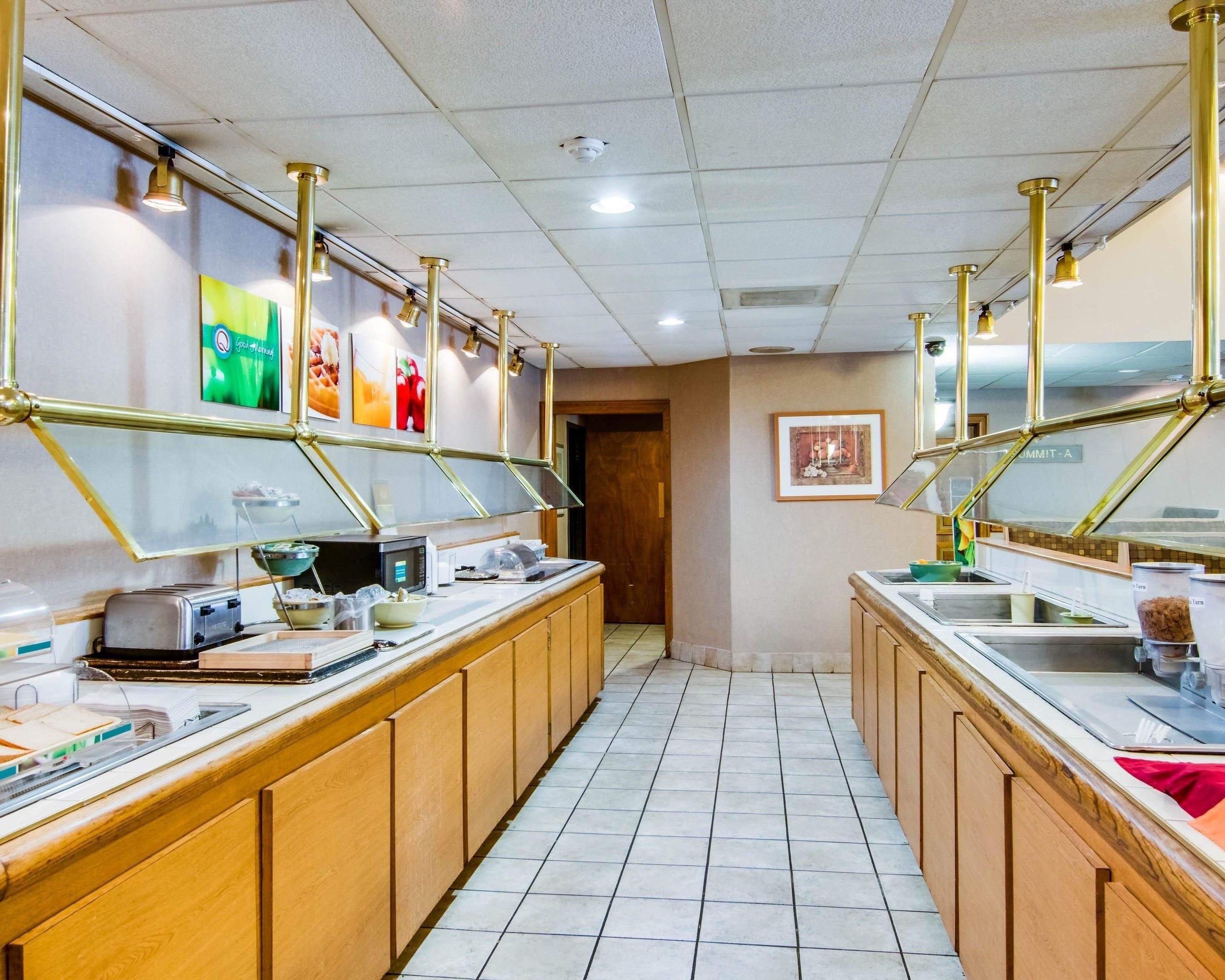 A long, narrow kitchen with wooden cabinets and stainless steel appliances. There are overhead lights and a microwave on the counter.