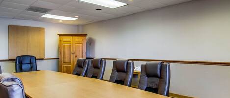Un salón de conferencias con una larga mesa, seis sillas de cuero, un aparador de madera e iluminación empotrada en el techo.