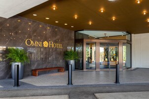 L’entrée de l’hôtel Omni, avec sa façade en marbre, un banc et des plantes en pot.