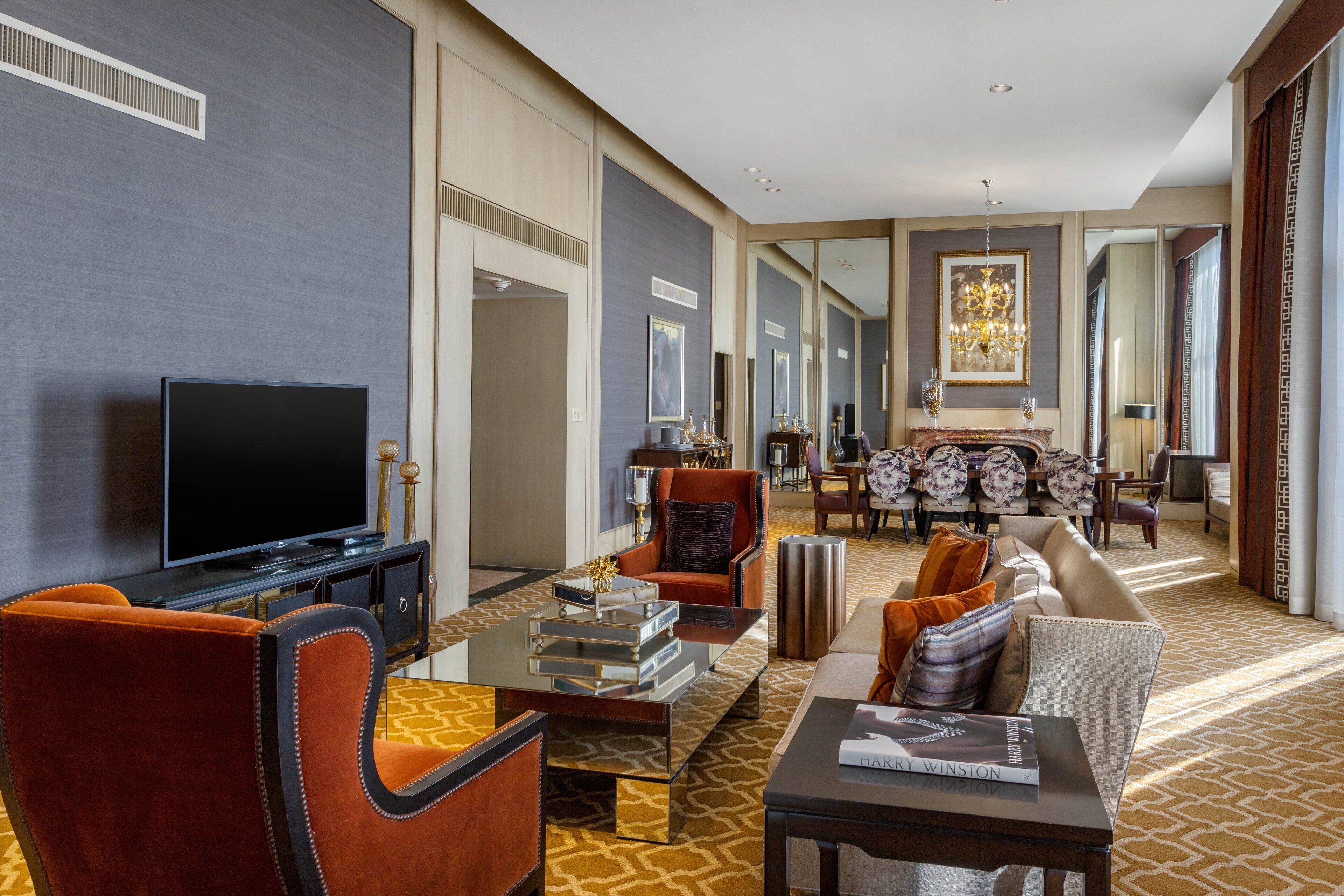 A spacious living room with a flat-screen TV, comfortable seating, a dining area with a chandelier, and a large mirror reflecting the space.