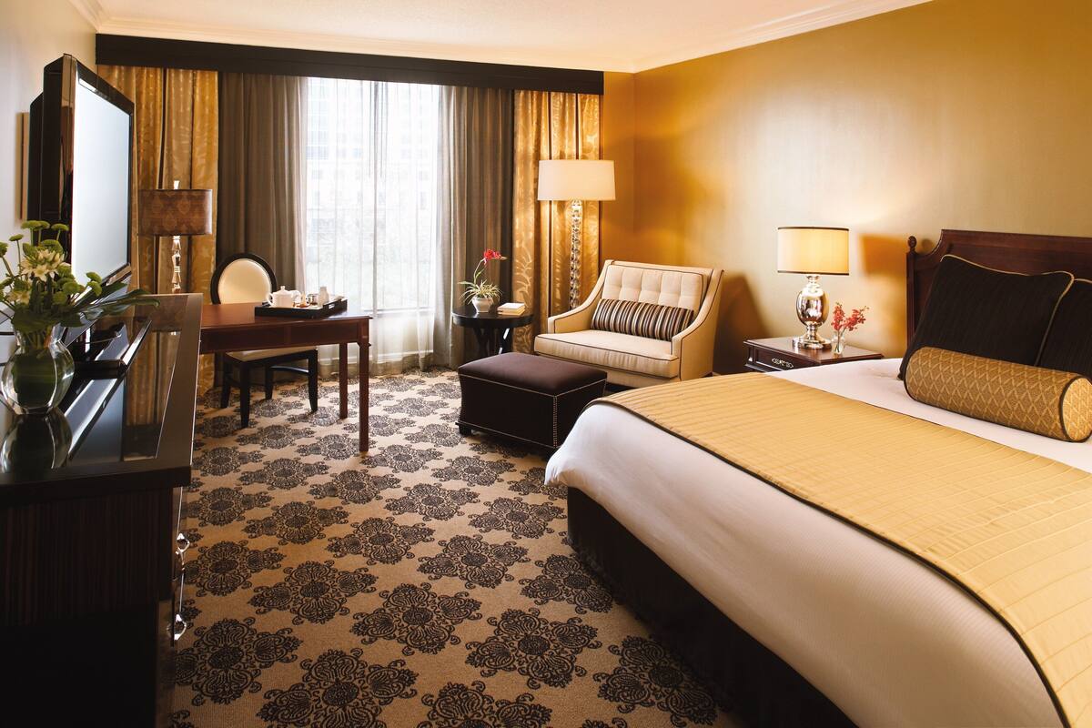 A hotel room with a large bed, a desk with a chair, a television, and a lamp.