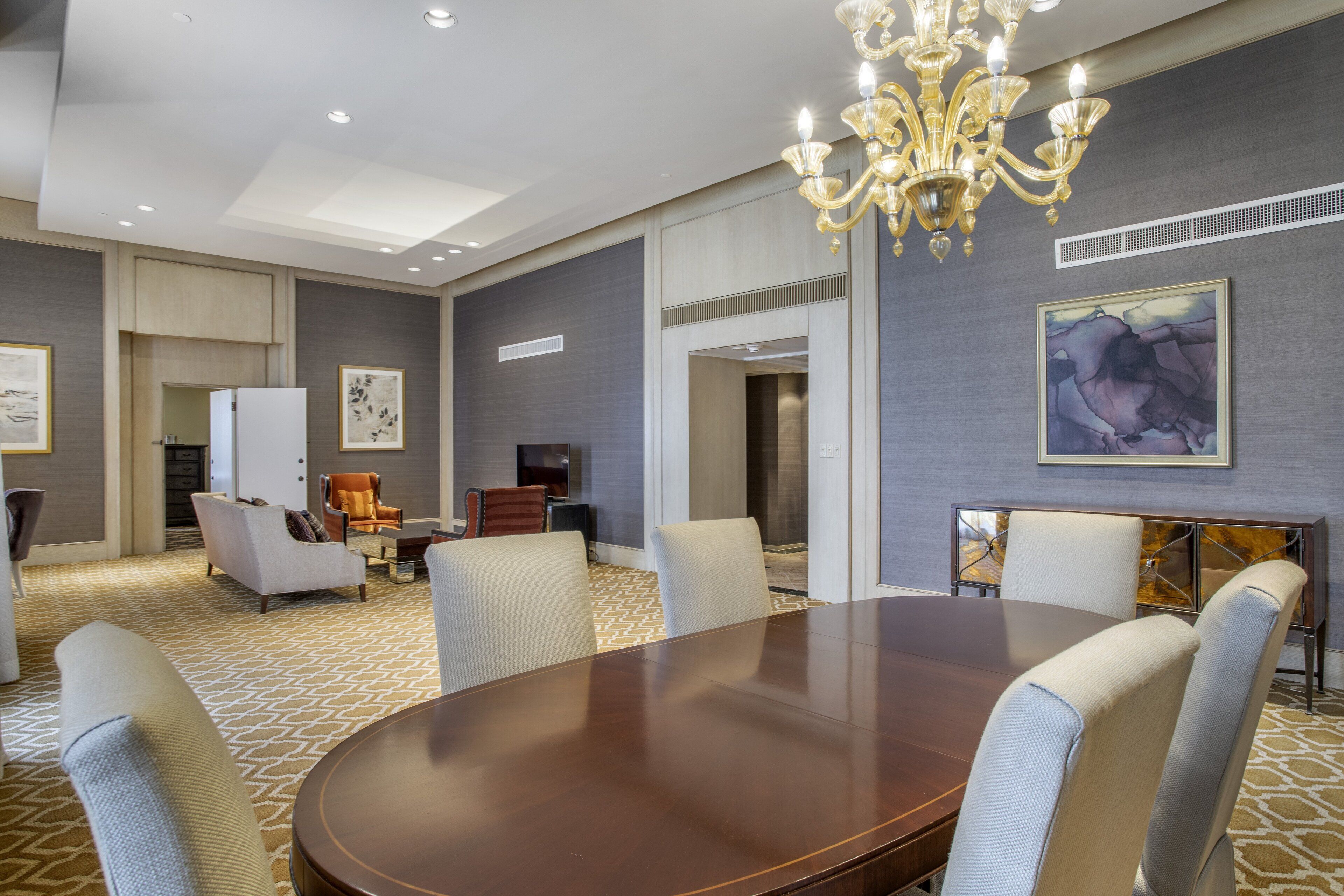 A conference room with a large table, chairs, a chandelier, and artwork on the walls.