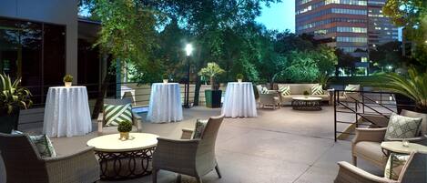 An outdoor patio area with wicker furniture, round tables, and potted plants.