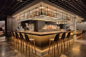 Zona de bar moderna con una isla central, taburetes y una vitrina de vidrio llena de botellas.