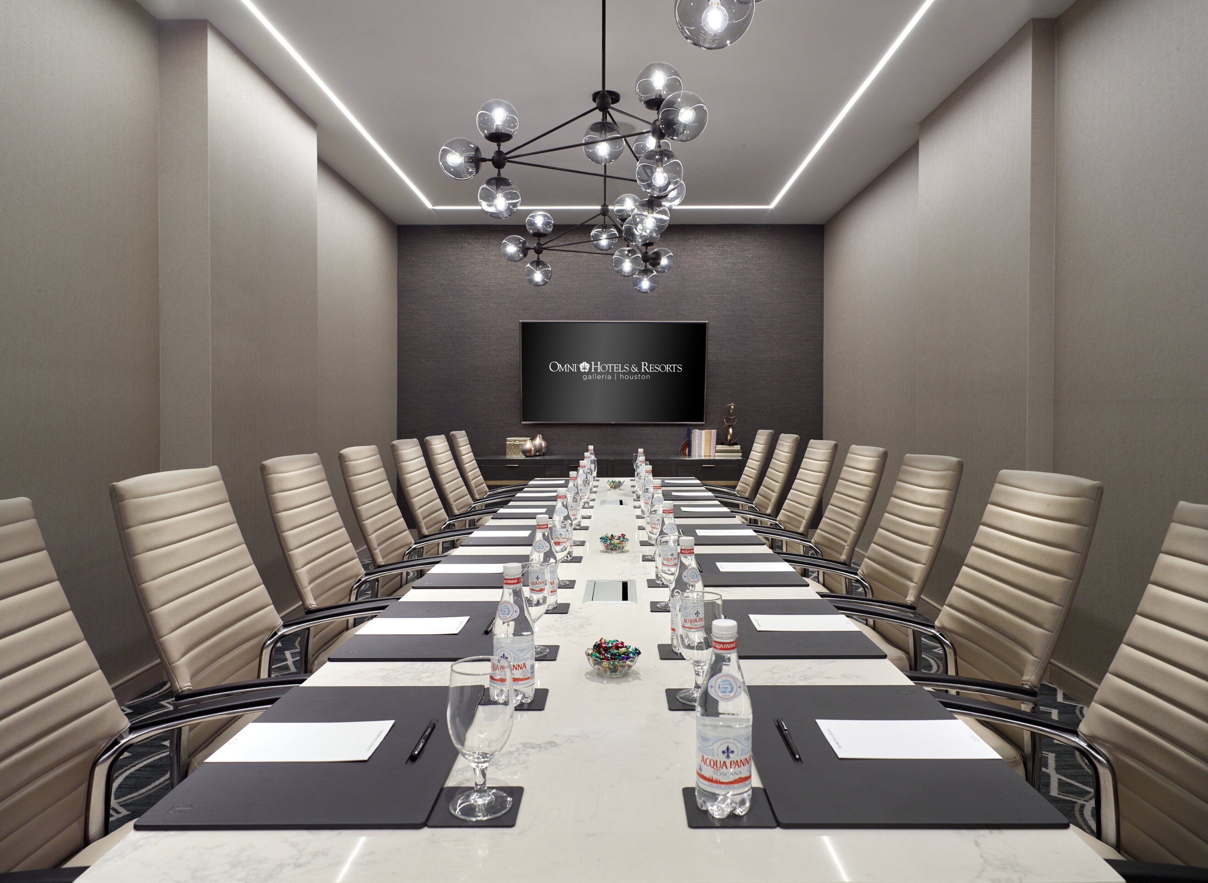 Ein Konferenzraum mit einem langen Tisch, Stühlen, Wasserflaschen und einem Fernsehbildschirm, der 'OMNI HOTELS & RESORTS' anzeigt.