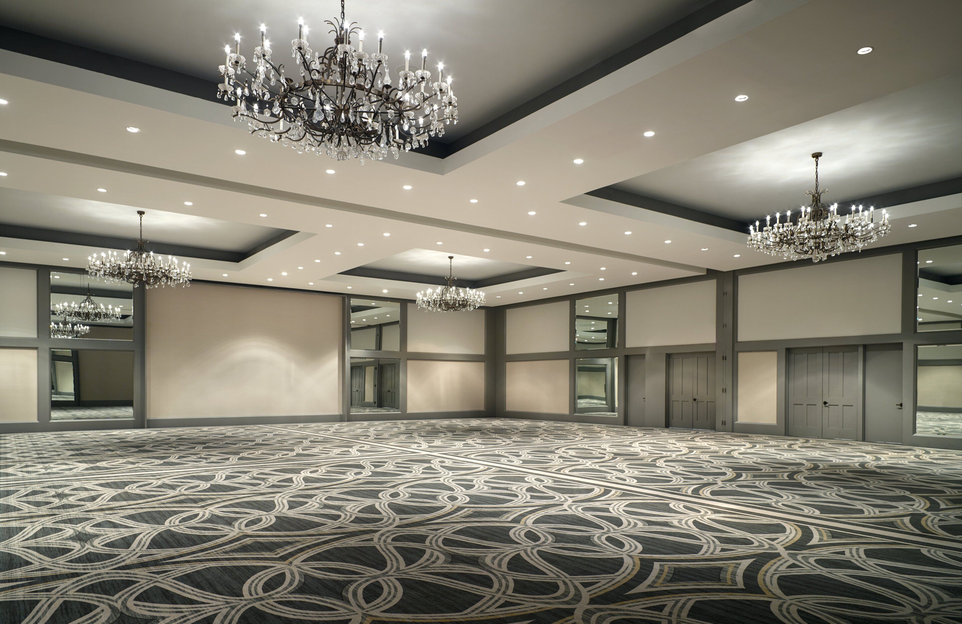 Amplia habitación de hotel con alfombra estampada, varios candelabros y un espejo grande que refleja el espacio.