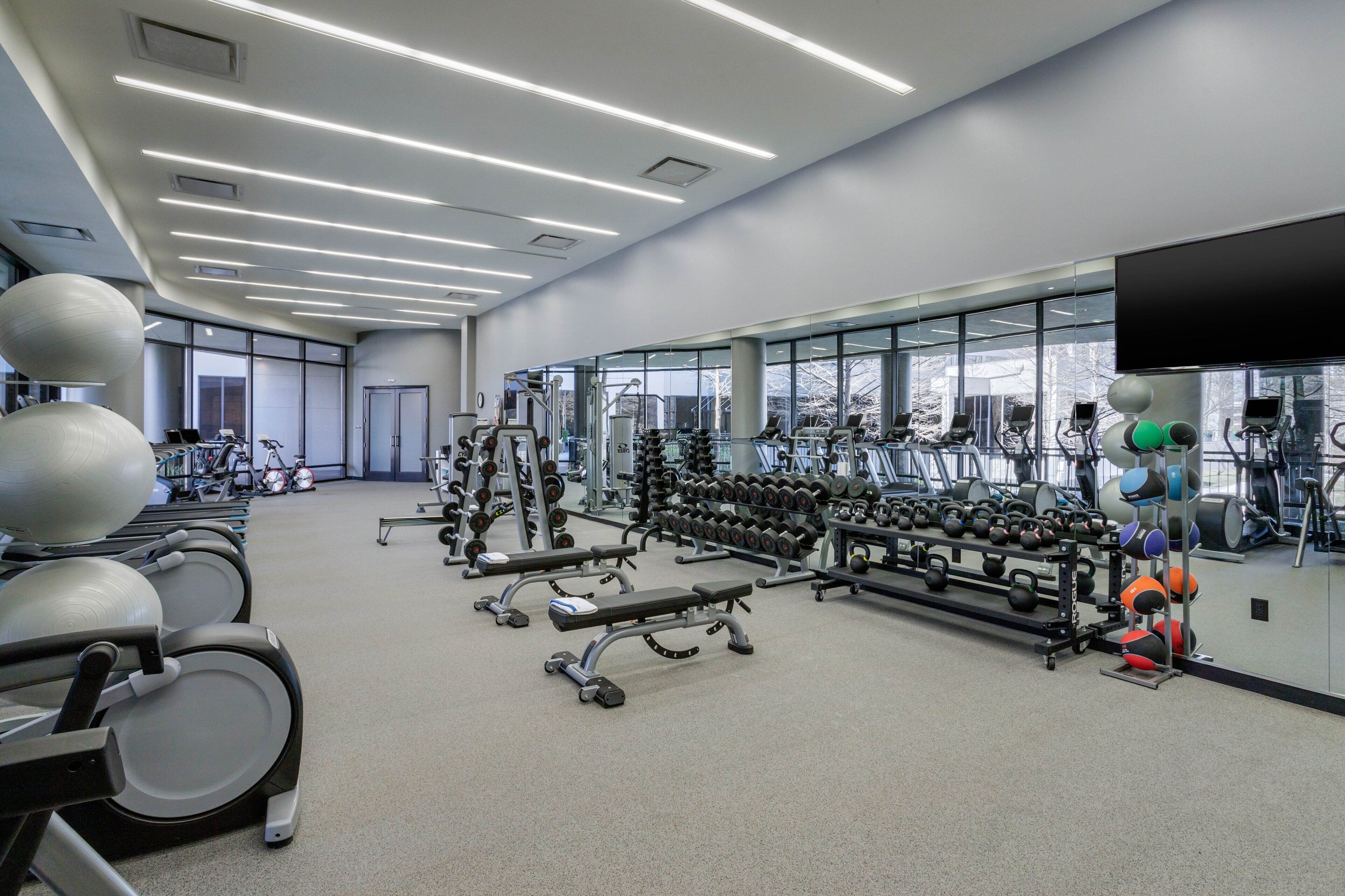 A modern gym with various exercise equipment, large windows, and a clean, spacious layout.