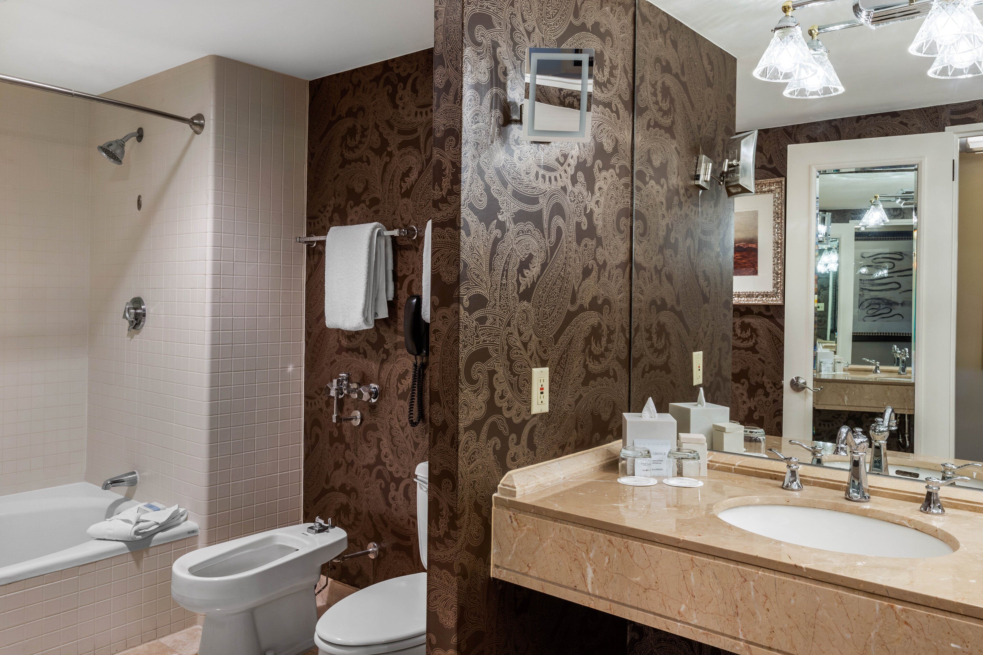 A bathroom with a bathtub, toilet, bidet, and a large mirror.
