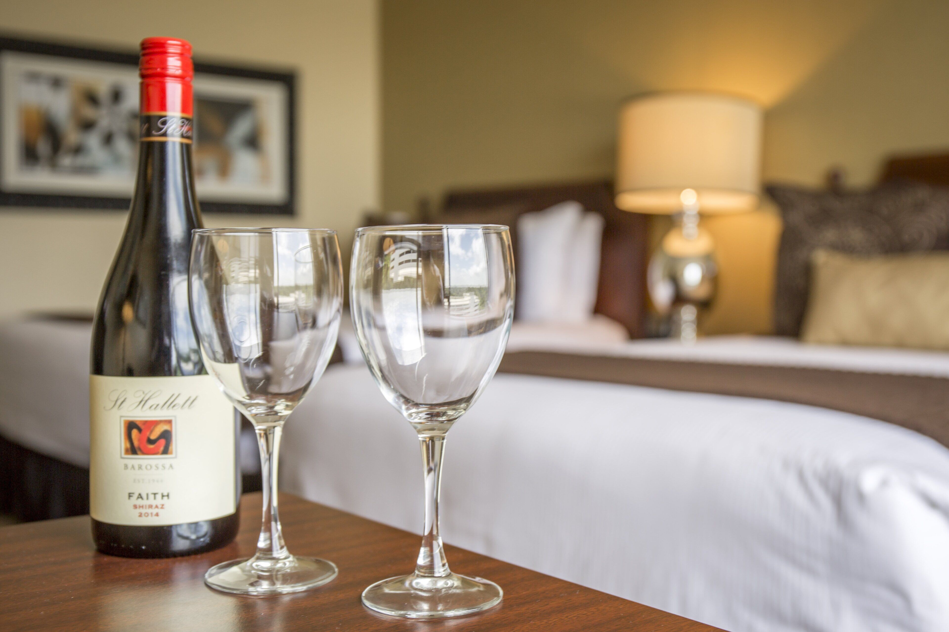 Een hotelkamer met een bed, een nachtkastje met een fles wijn en twee glazen.