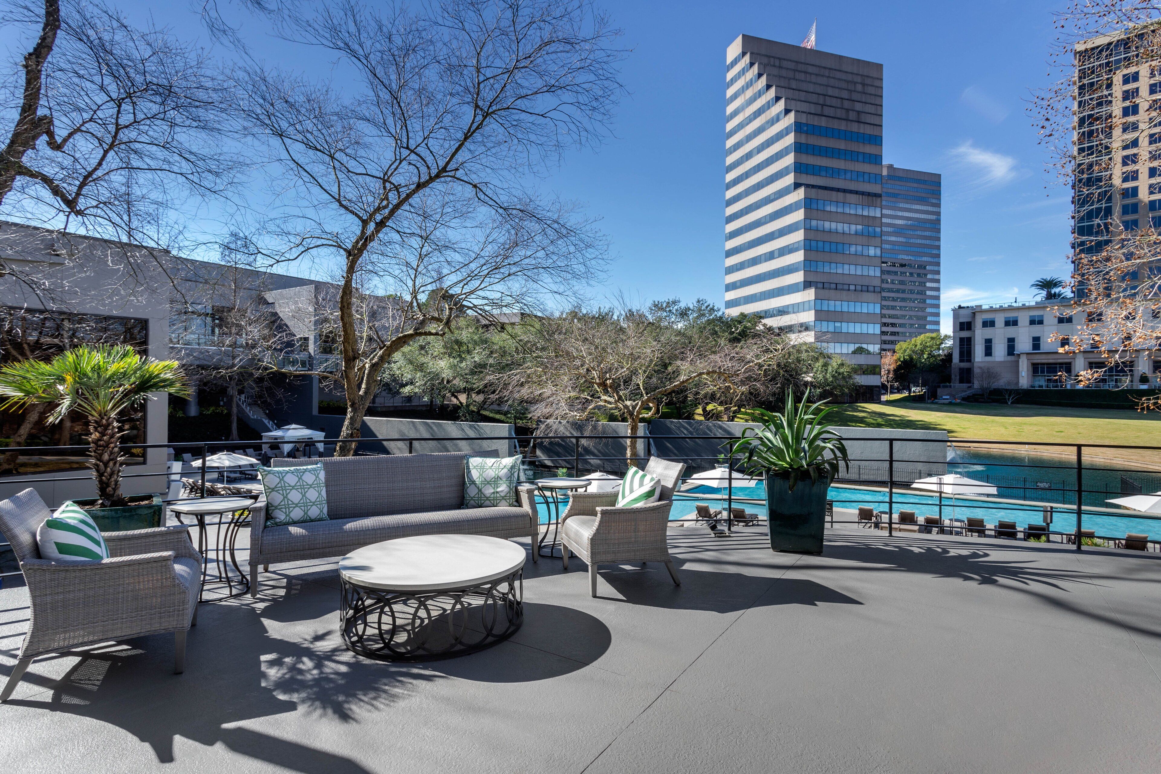 A rooftop patio with outdoor furniture, a pool, and city buildings in the background.