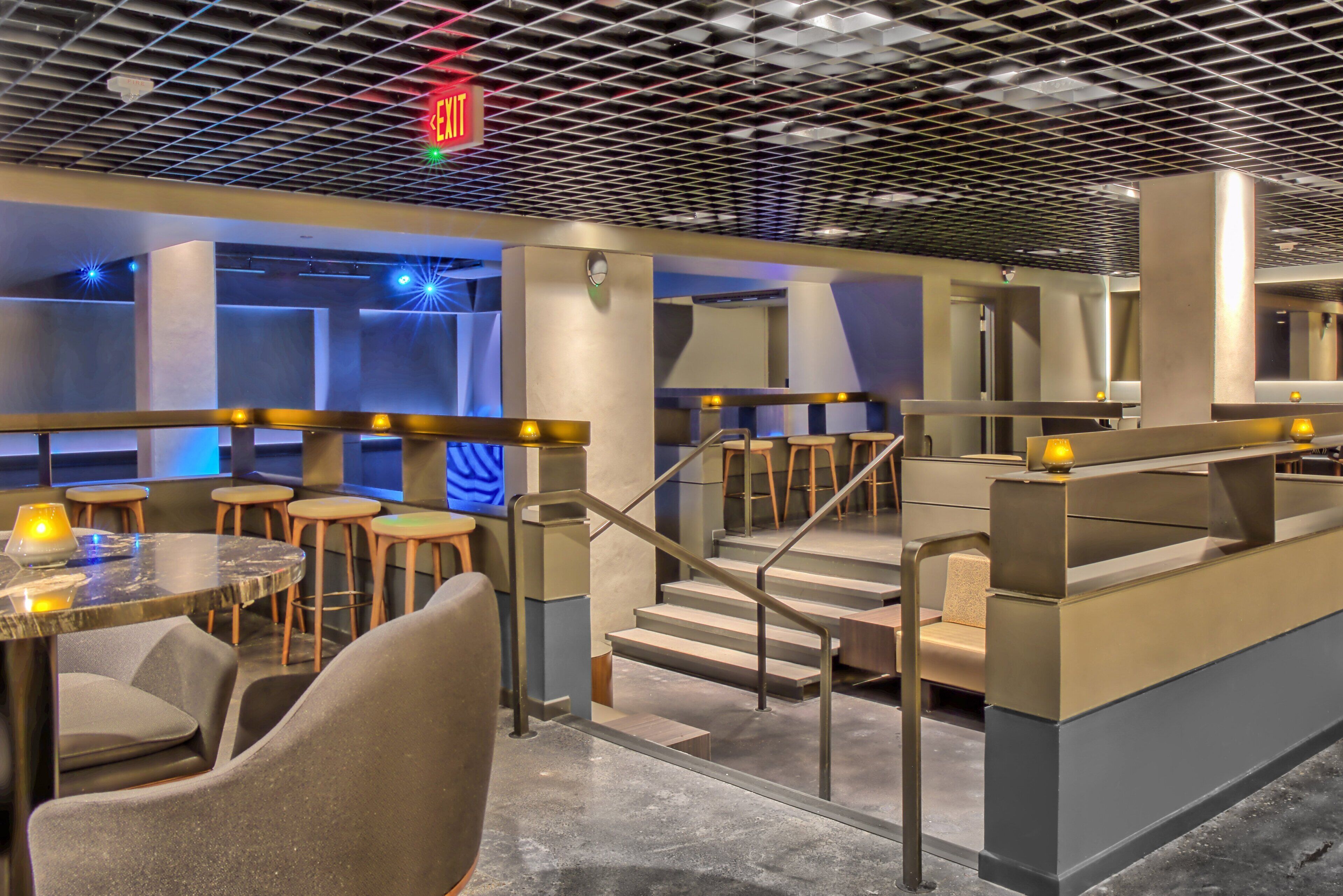 A modern bar area with seating, a staircase, and a visible exit sign.