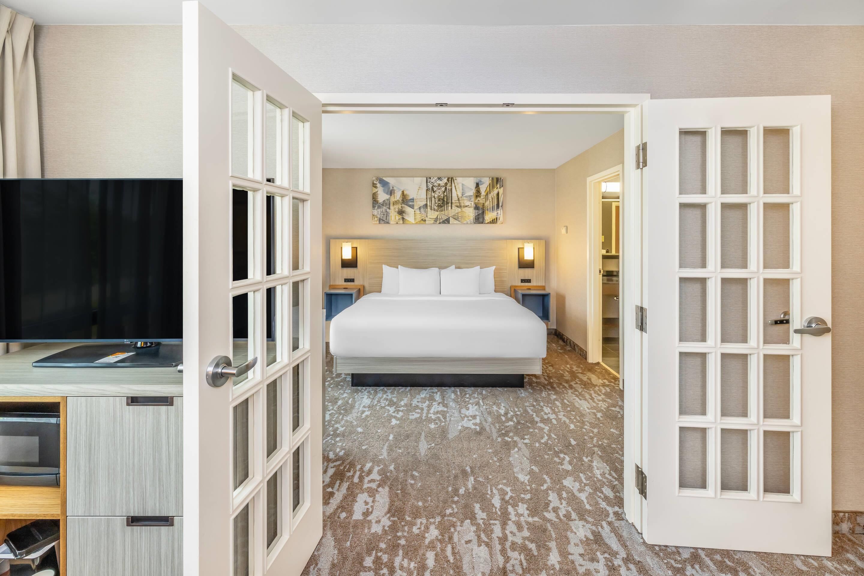 Une chambre d’hôtel avec un lit, un bureau équipé d’un ordinateur, une télévision et un tableau accroché au mur.