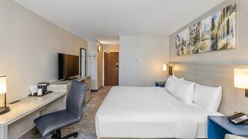 A hotel room with a bed, desk, chair, TV, and artwork on the wall.