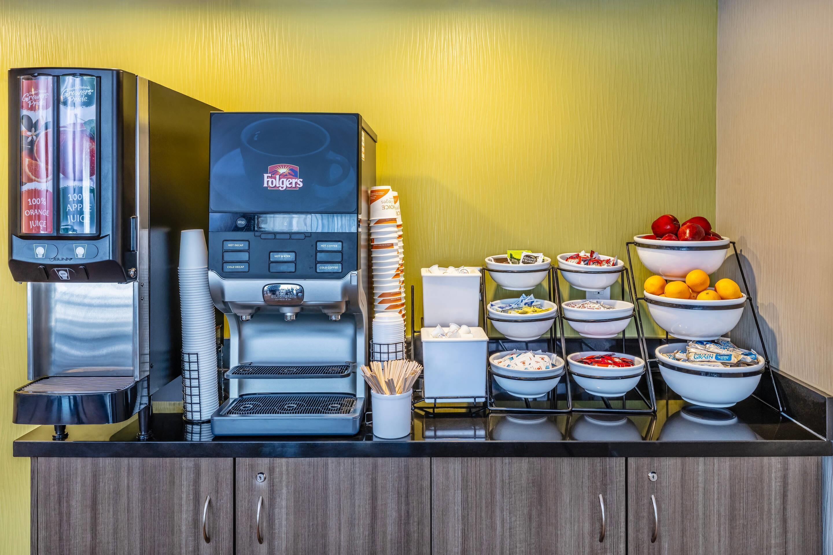Una estación de autoservicio para bebidas, con una máquina de café Folgers y un dispensador de jugo.
