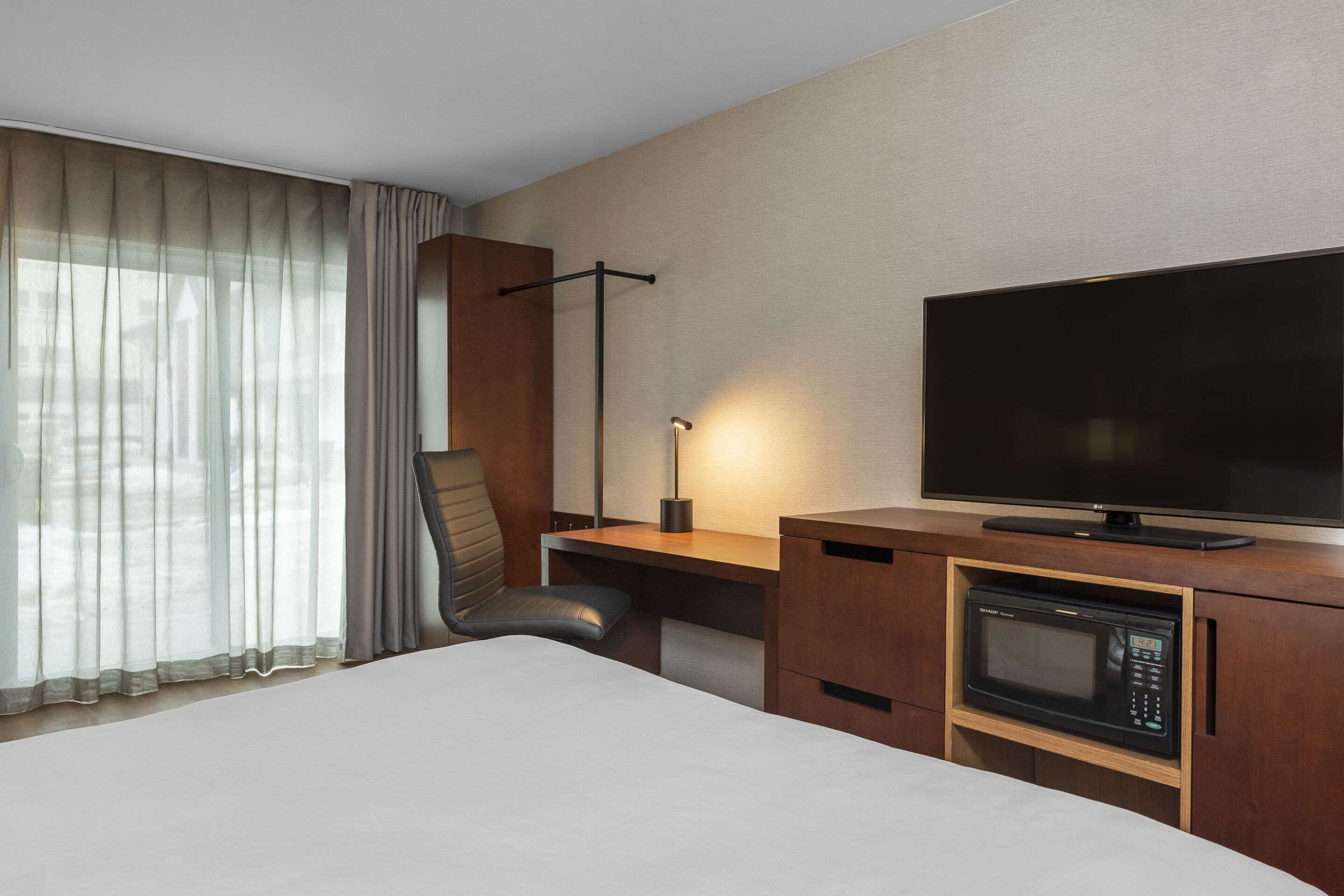 Una habitación de hotel con una cama, un escritorio con televisor, microondas y una silla.
