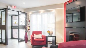 A hotel lobby with a red sofa, a red armchair, a TV on a black stand, and a glass door labeled "OFFICE". - Comfort Inn (Fredericton)