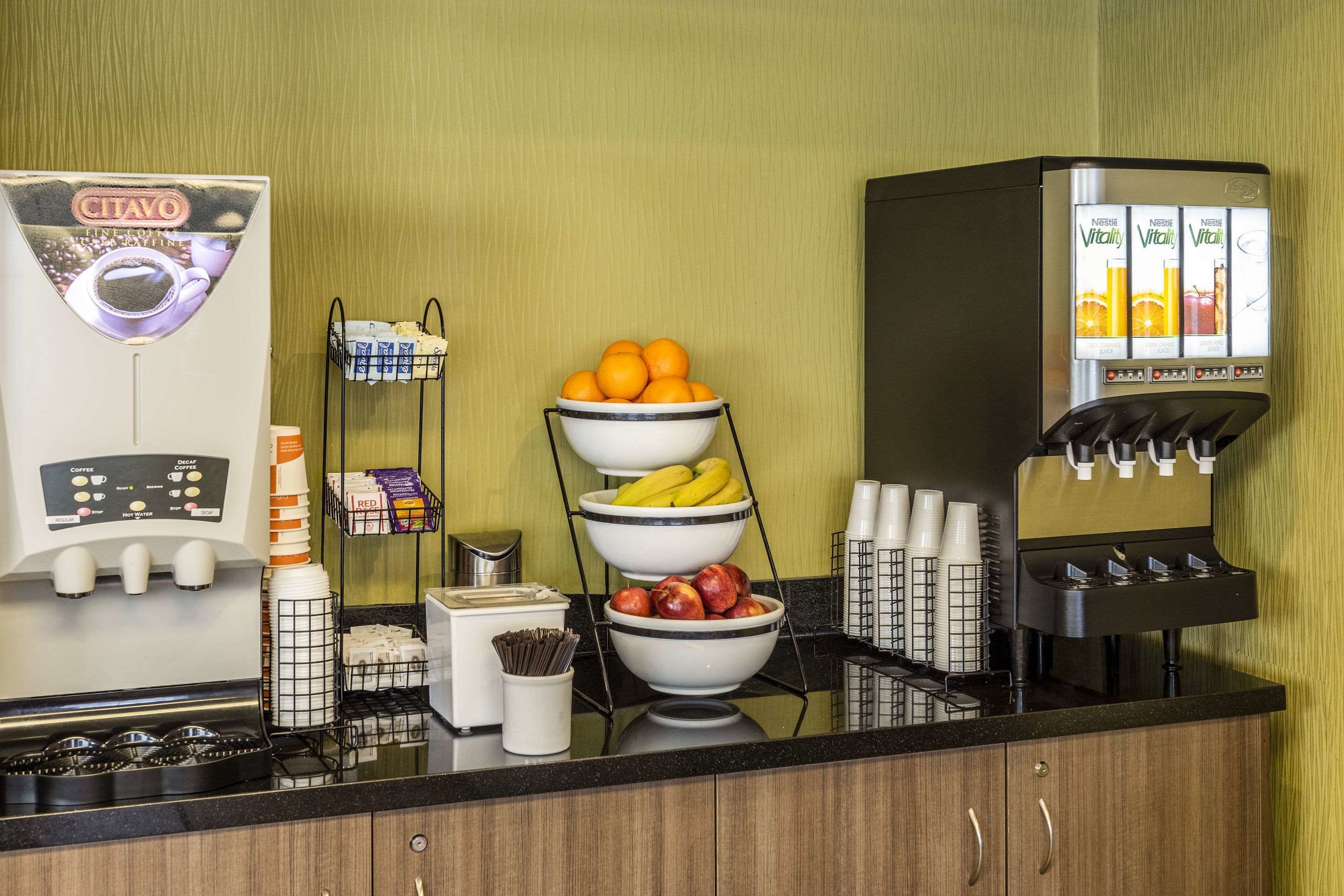 Una estación de café con una cafetera, fruteros y un dispensador de zumo.