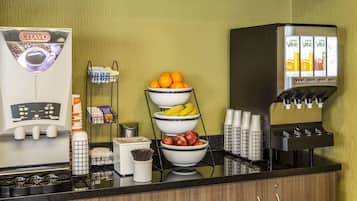 Una estación de café con una cafetera, fruteros y un dispensador de zumo.