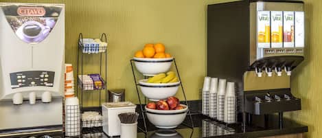 Una estación de café con una cafetera, fruteros y un dispensador de zumo.
