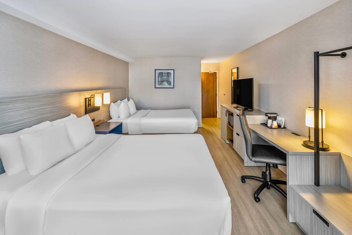 A hotel room with two beds, a desk, a TV, and a lamp.