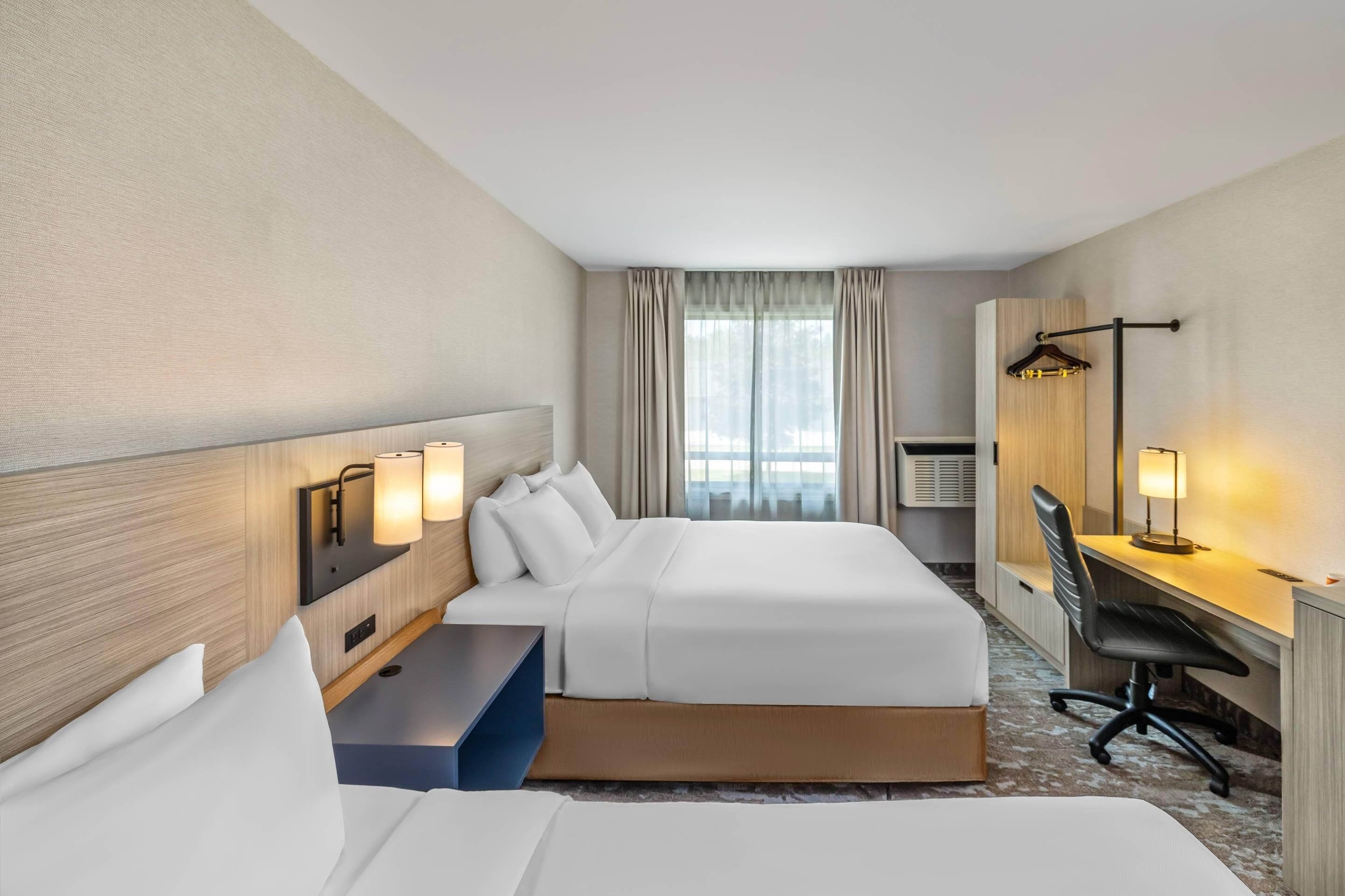 Hotellihuone, jossa on kaksi sänkyä, työpöytä, tuoli ja vaatekaappi.