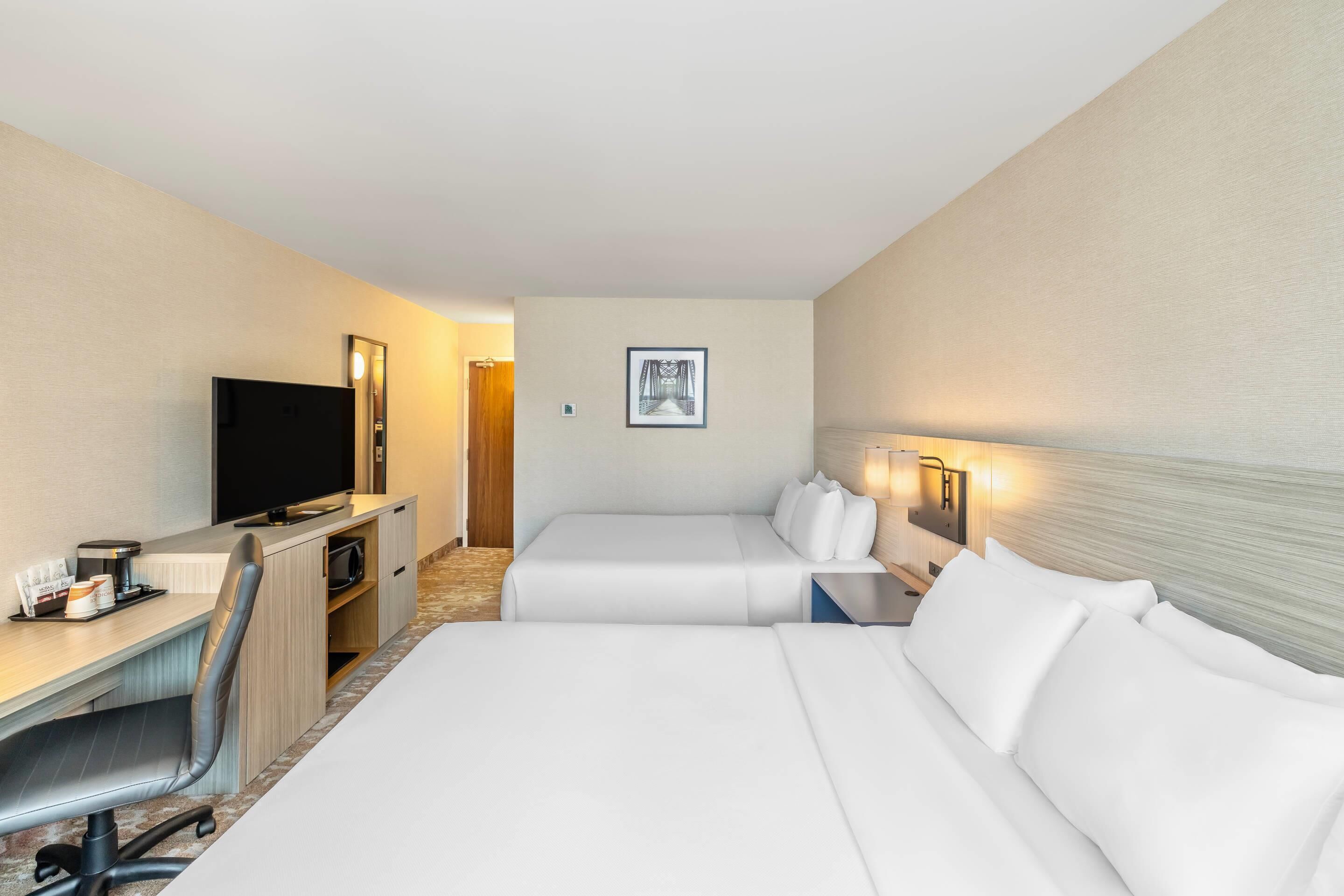 A hotel room with two beds, a desk with a computer, a TV, and a coffee machine.