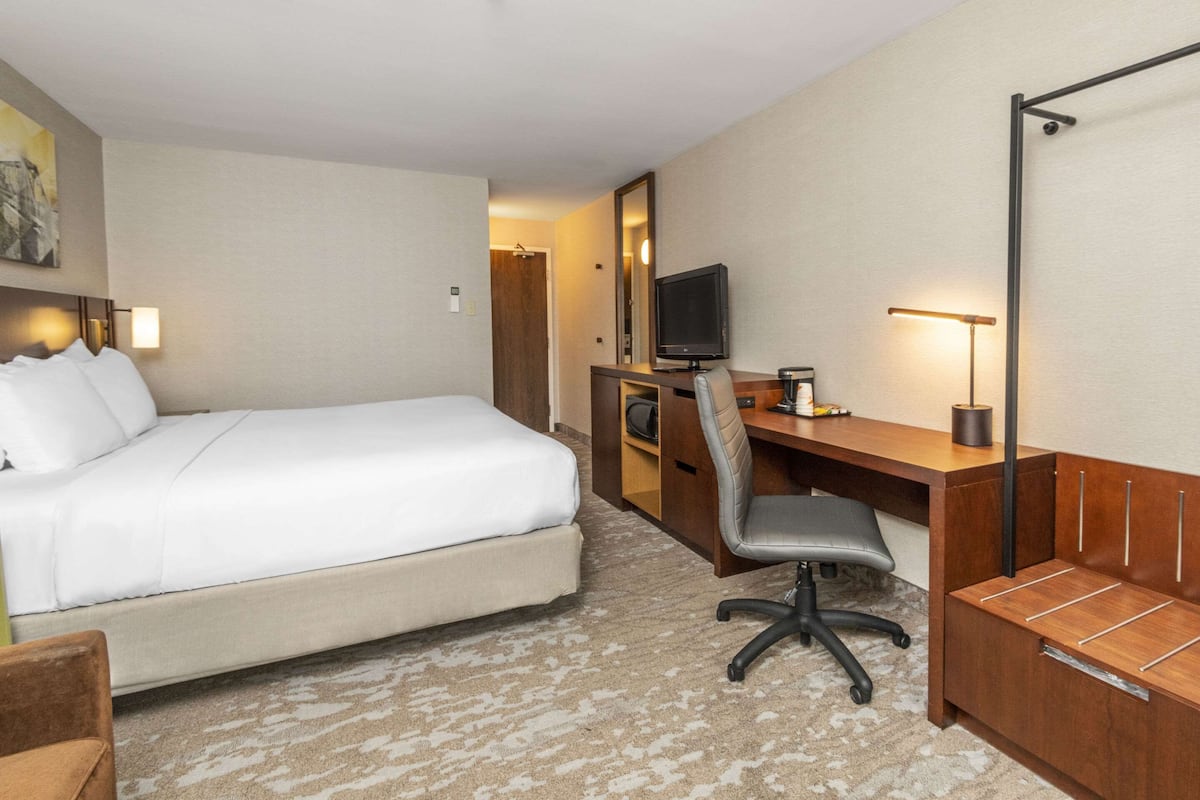 A hotel room with a bed, desk, chair, TV, and a small seating area.