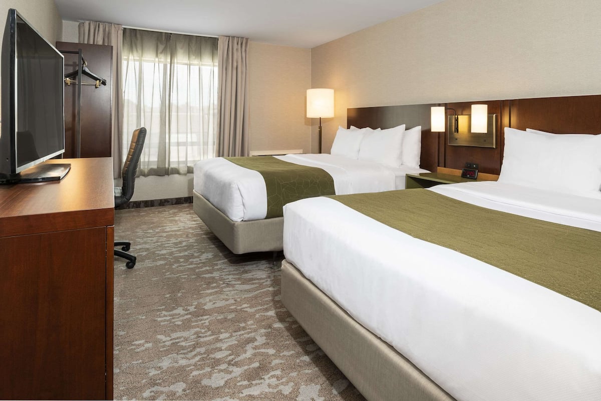 A hotel room with two beds, a desk with a computer, a chair, a lamp, and a window with curtains.