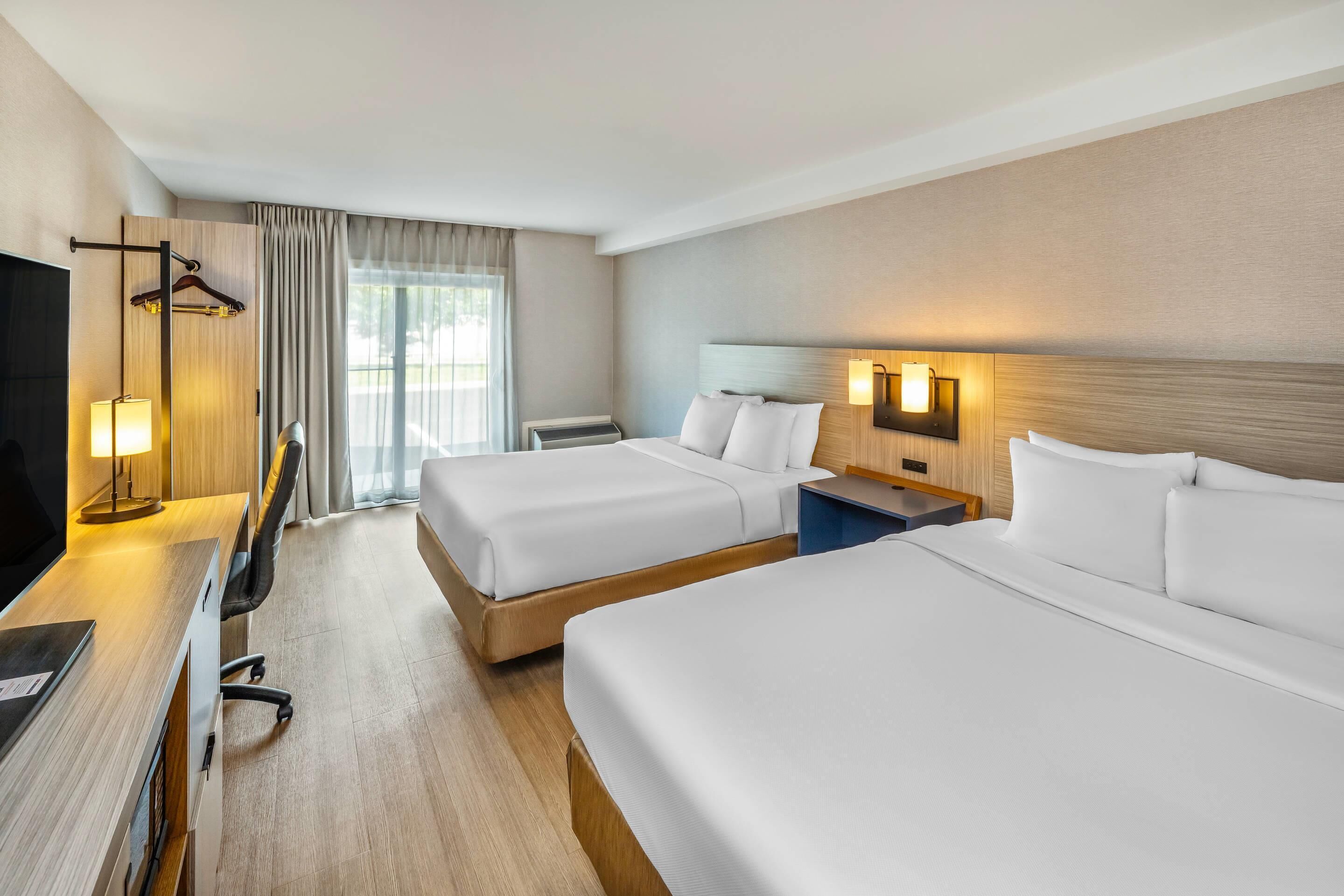 A hotel room with two beds, a desk with a computer, a TV, and a lamp.