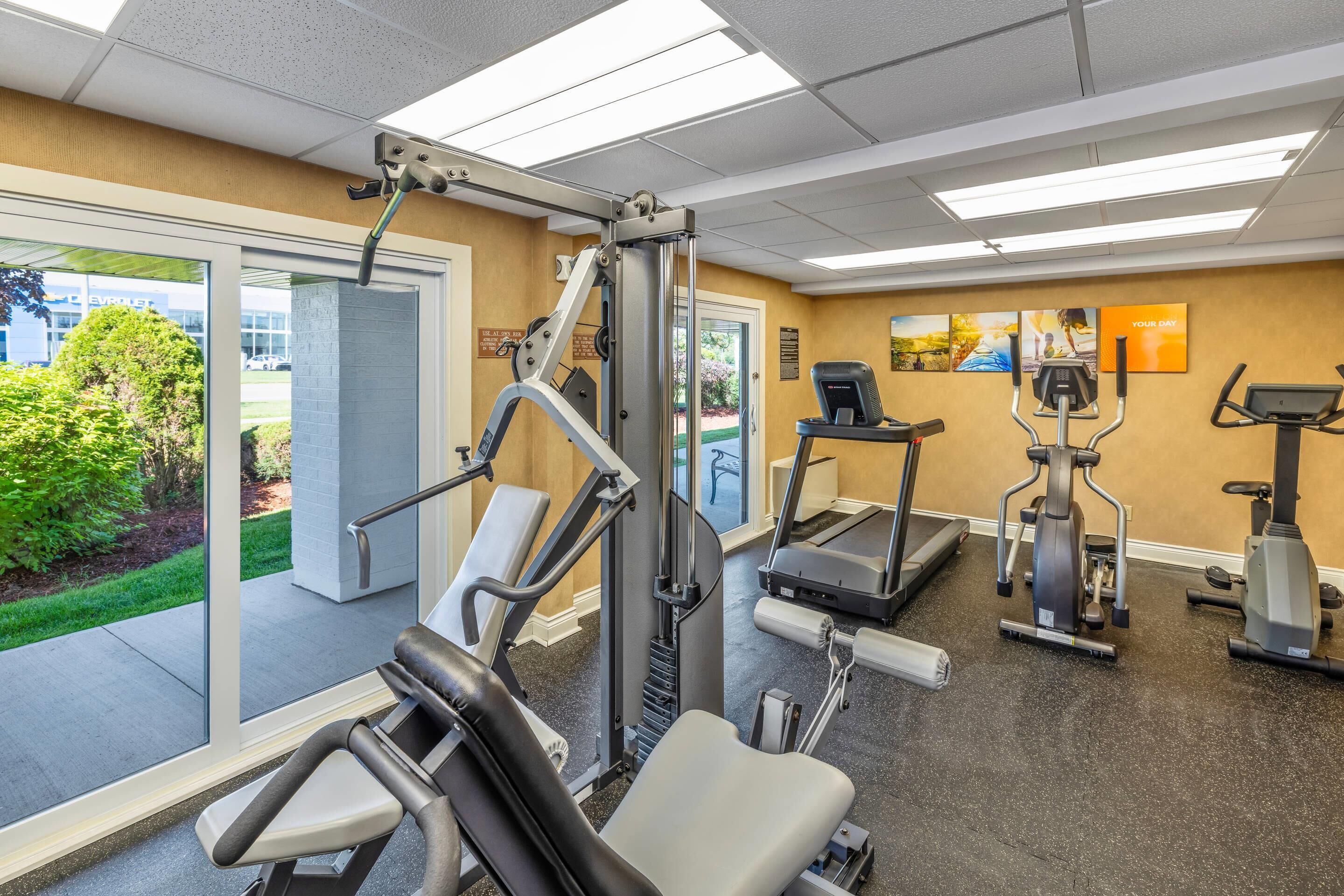 A gym with cardio machines, weight machines, and a large window providing a view of the outdoors.