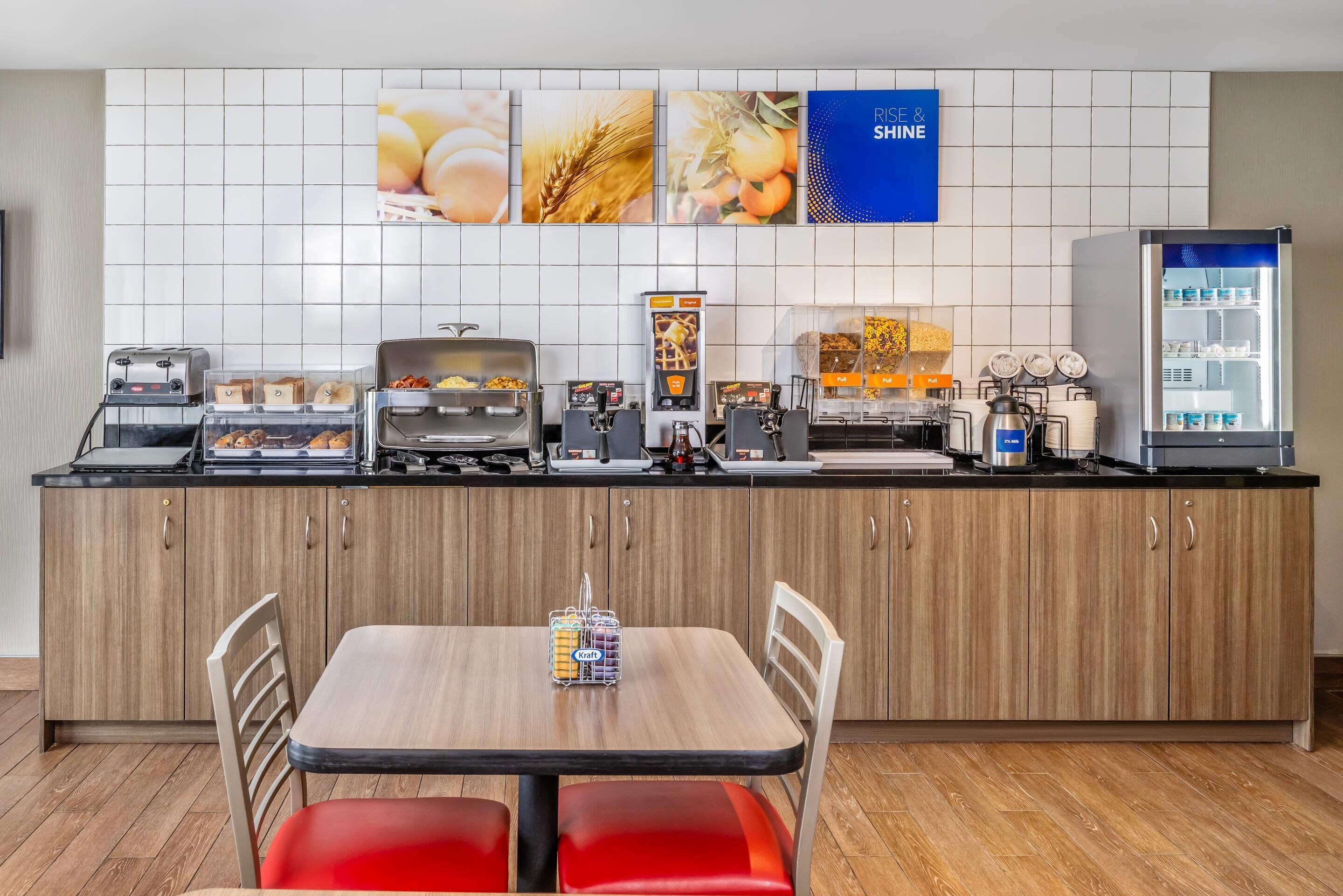Eine moderne Küche mit Kochinsel, ausgestattet mit diversen Geräten wie Kaffeemaschine, Toaster und Wasserkocher. Rechts befindet sich ein Kühlschrank und eine wandmontierte Kaffeestation.