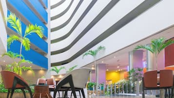 Un moderno vestíbulo de hotel con techo curvo, zona de estar con sillas y mesas, y plantas de palma decorativas.