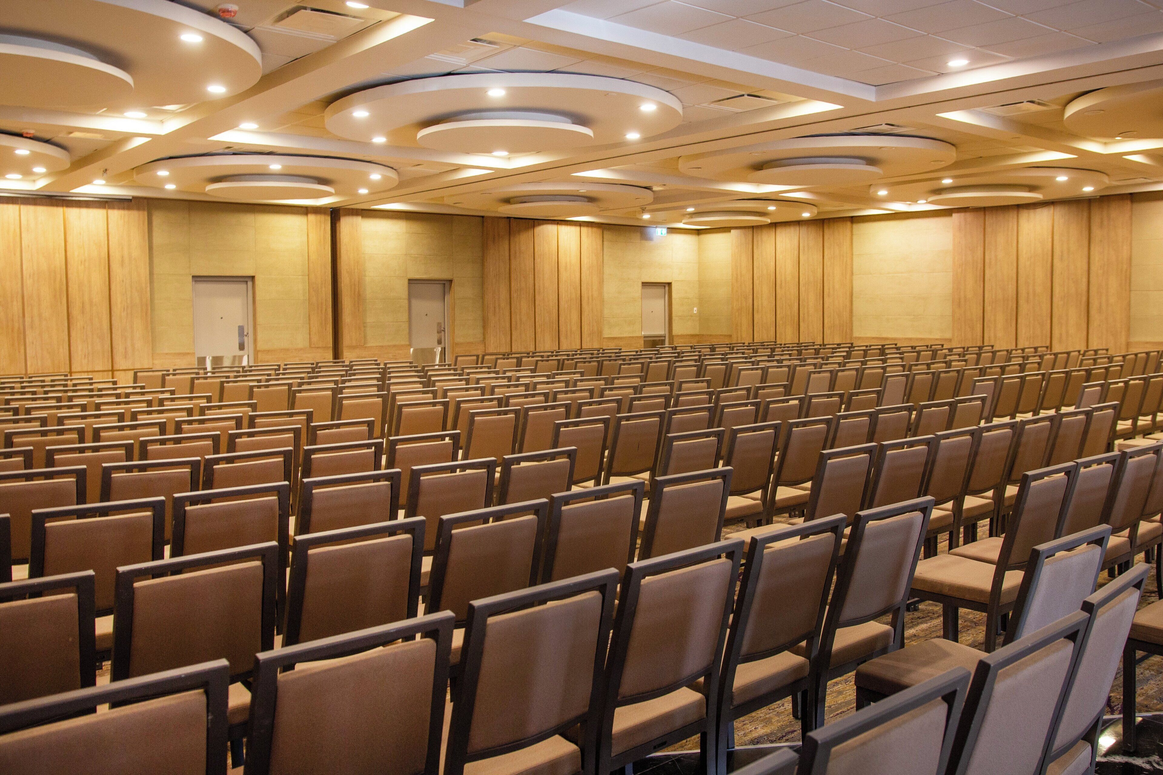 Un'ampia sala conferenze con file di sedie, pareti rivestite in legno e illuminazione a soffitto incassata.