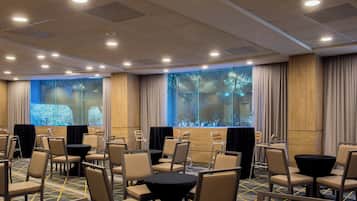 Une salle de conférence dotée de plusieurs tables et chaises, de grandes fenêtres avec des rideaux et d’un plafond équipé d’un éclairage encastré.