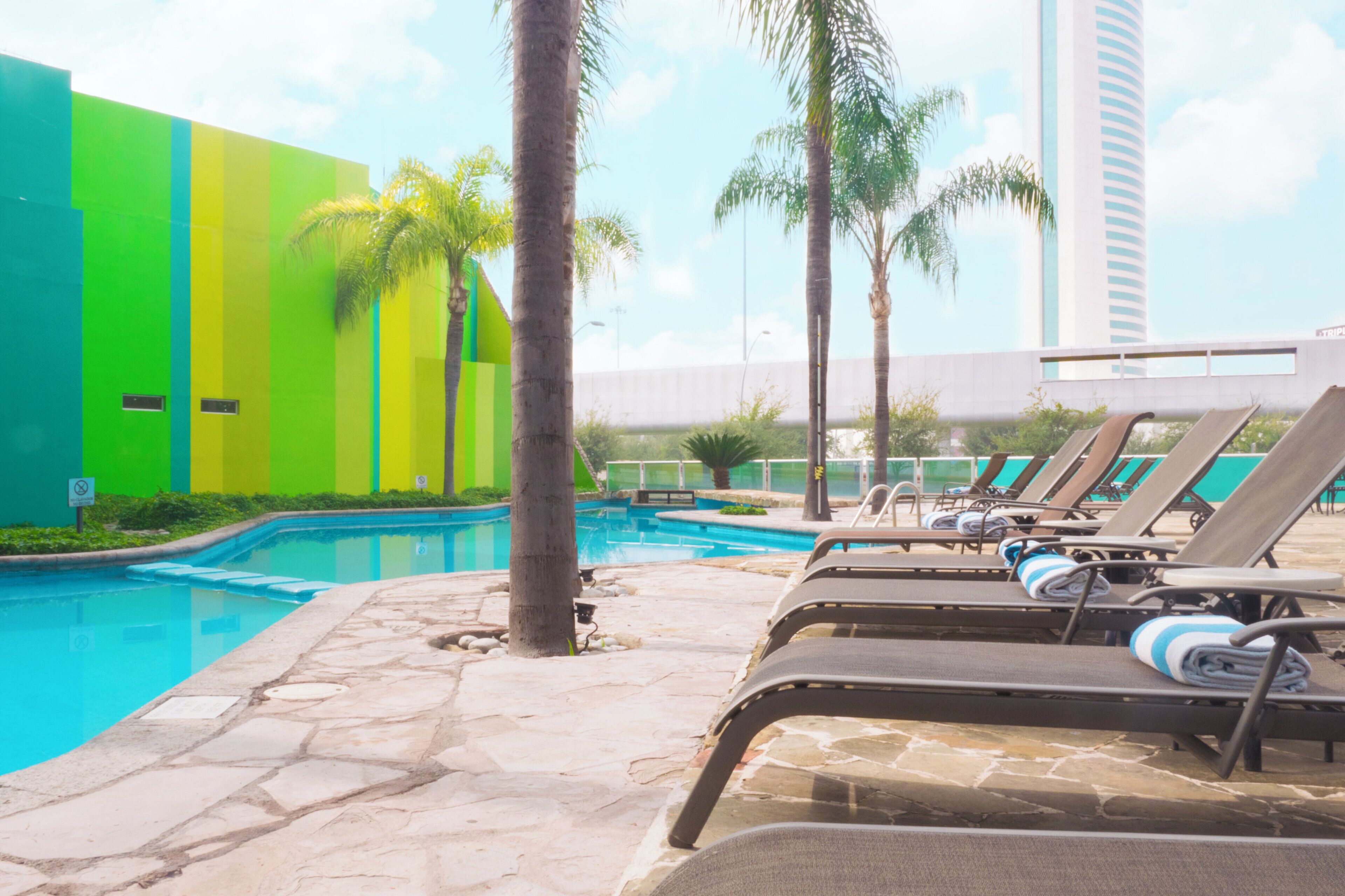 A swimming pool area with lounge chairs and palm trees.