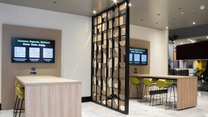 Een moderne receptie met een houten receptiebalie, een bar met zitplaatsen en twee digitale schermen waarop QR-codes voor diensten staan.