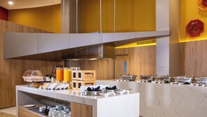 Een buffetopstelling met diverse gerechten en bakken, een koffiehoek en een zithoek met stoelen.