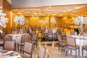 Uma sala de banquetes com mesas redondas, cadeiras e centros de mesa florais.