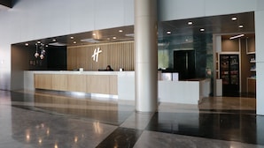 A modern hotel lobby with a reception desk, a large pillar, and a glass wall. - Holiday Inn Monterrey - Parque Fundidora by IHG (Monterrey)