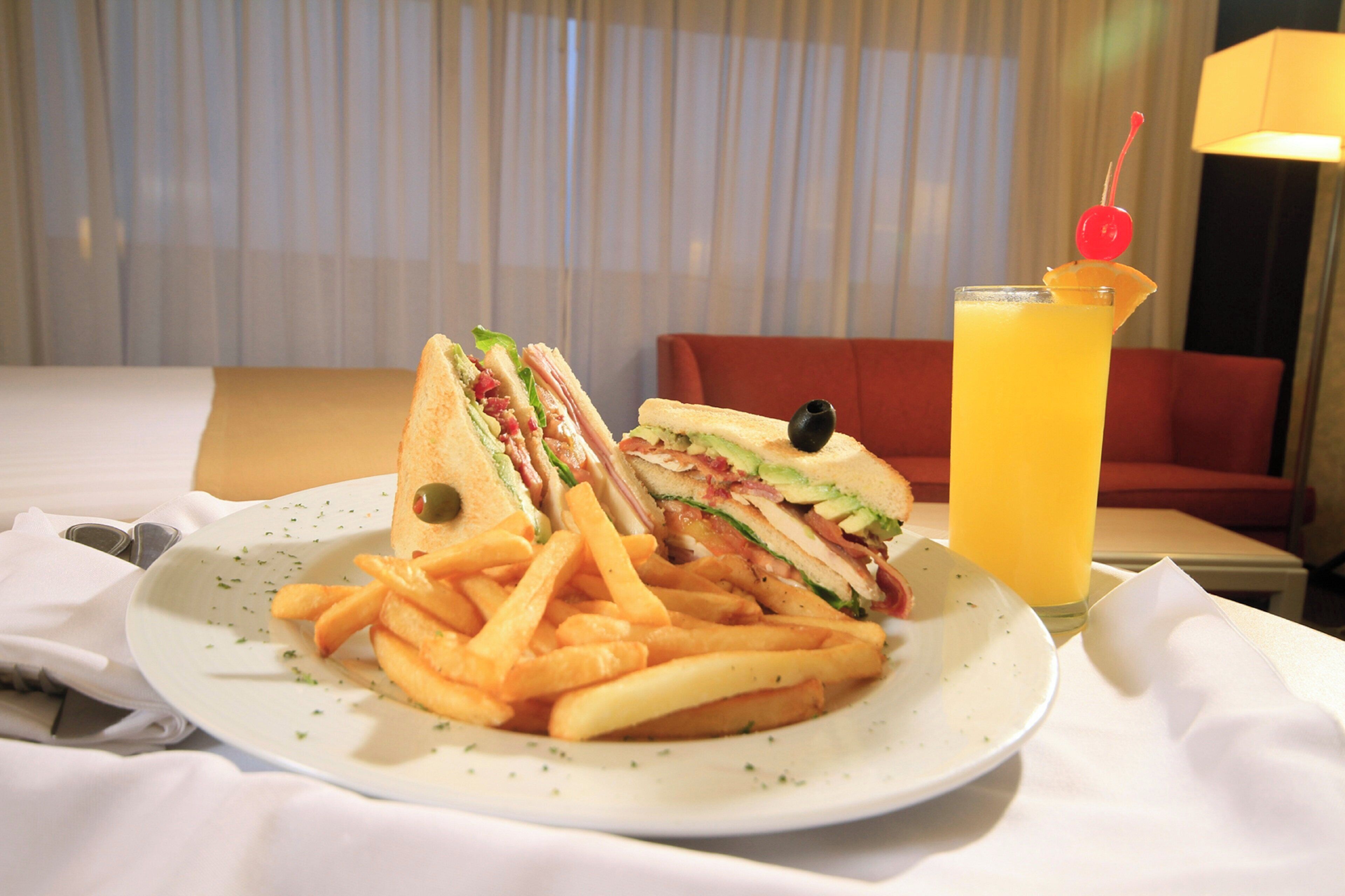 A plate with a sandwich and fries, a glass of orange juice, and a red couch in the background.