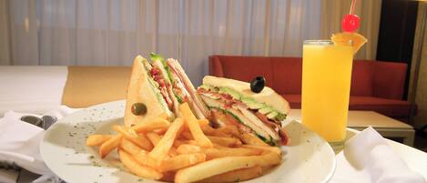 Un plato con un sándwich y papas fritas, un vaso de jugo de naranja y un sofá rojo al fondo.