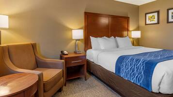 Quarto de hotel com cama, uma cadeira, mesa de cabeceira e duas luminárias fixadas na parede.